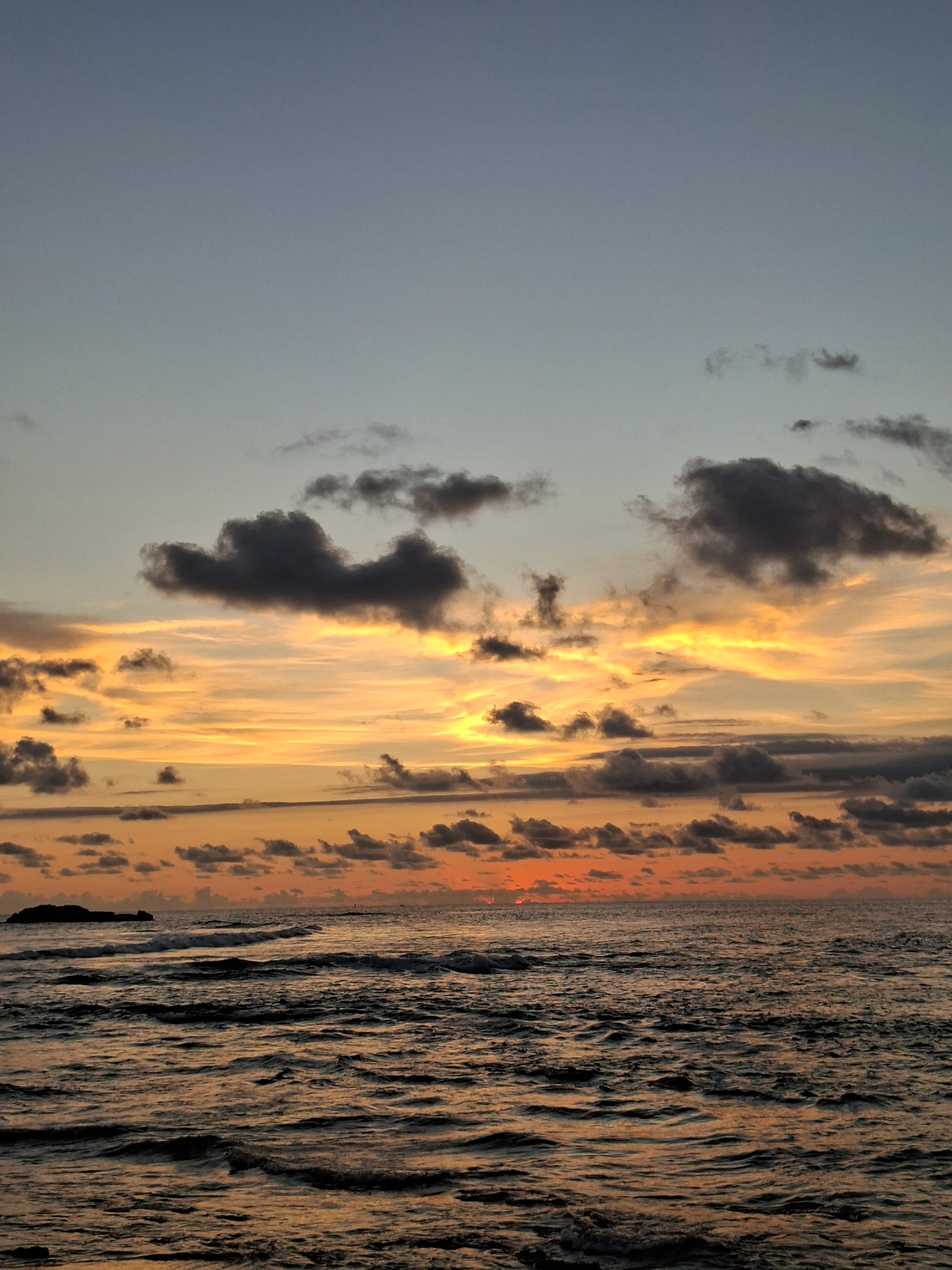 Sunset over the ocean, dark clouds and white foam along the shore
